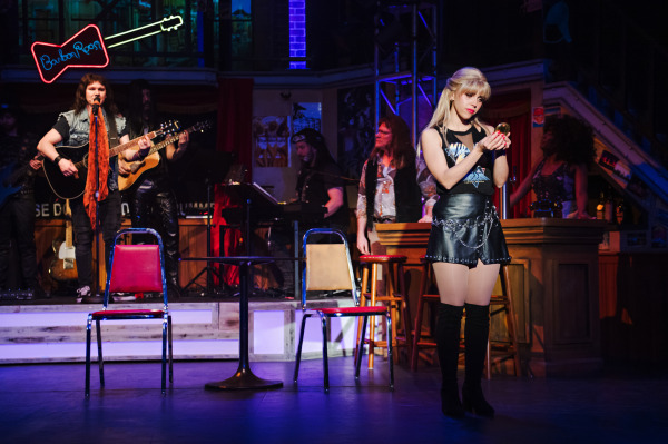 Production photo of Rock of Ages, showing two actors singing and playing guitar. 